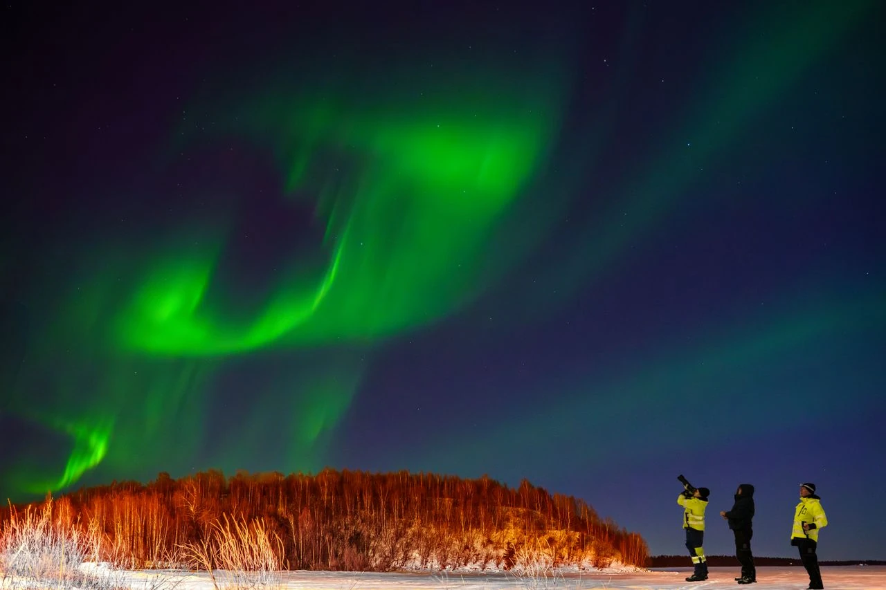 Viajeros observan una aurora boreal verde durante una excursión nocturna en un paisaje nevado